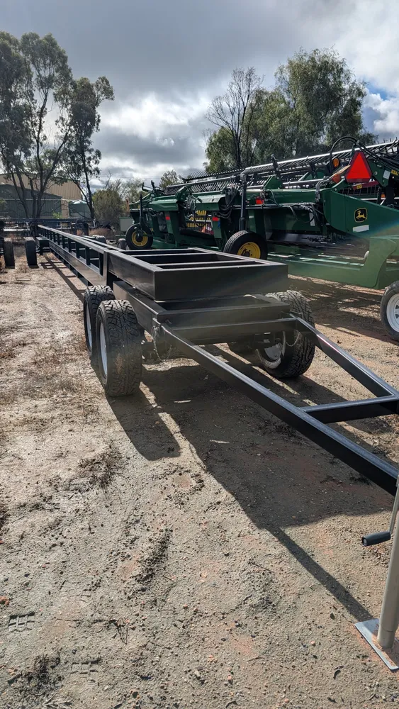 New comb trailer in the HFR yard at Swan Hill, three-quarter view from the drawbar end, with John Deere draper fronts behind it